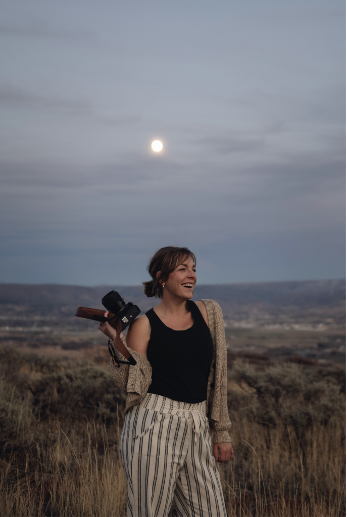 Ali stands in front of a rising full moon at twilight