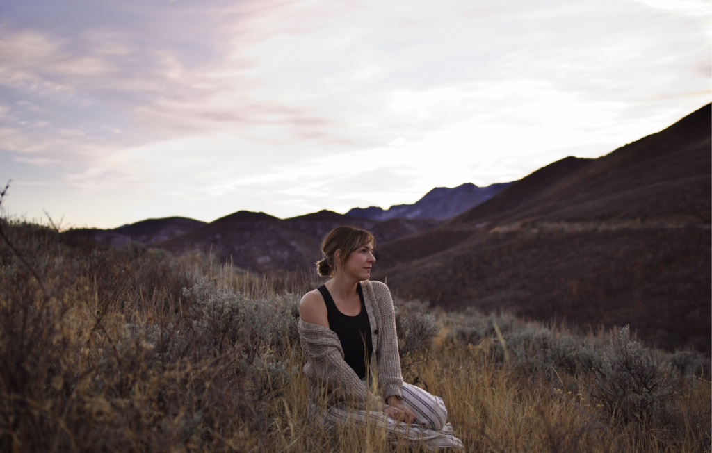 Ali sits in a field among mountains as twilight.