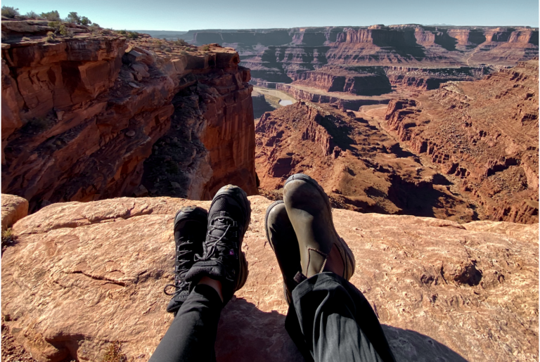Two sets of hiking boots sitting on the edge of a cliff overlooking Dead Horse State Park canyons